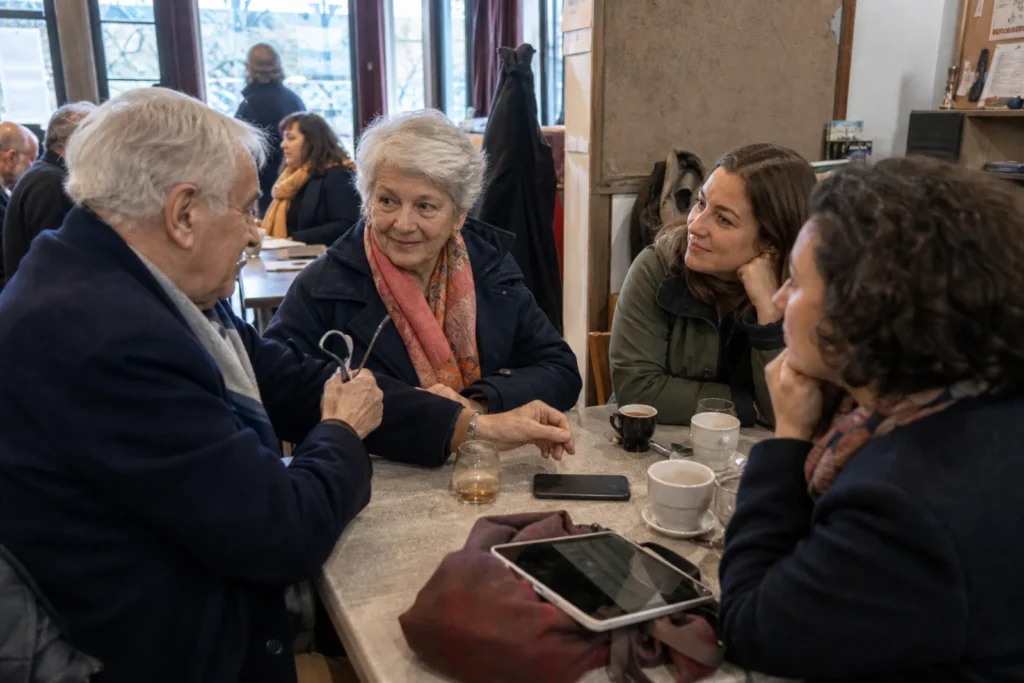 Un groupe intergénérationnel échange naturellement autour d’une table dans un café.