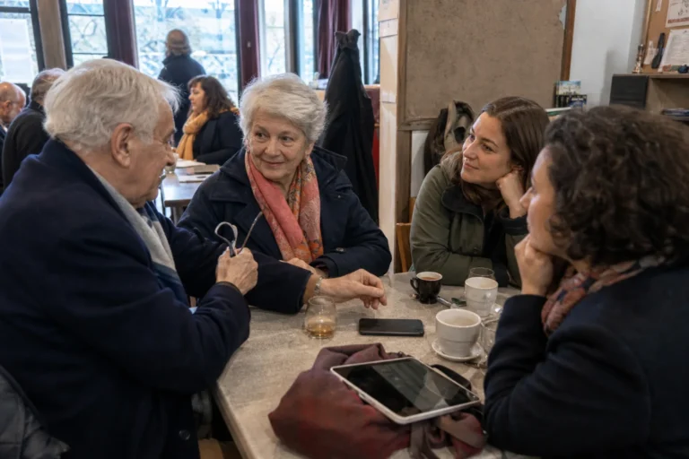 Un groupe intergénérationnel échange naturellement autour d’une table dans un café.